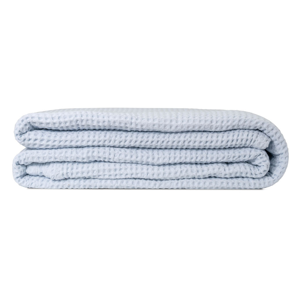 Cream waffle weave cotton throw blanket draped over the arm of a linen sofa